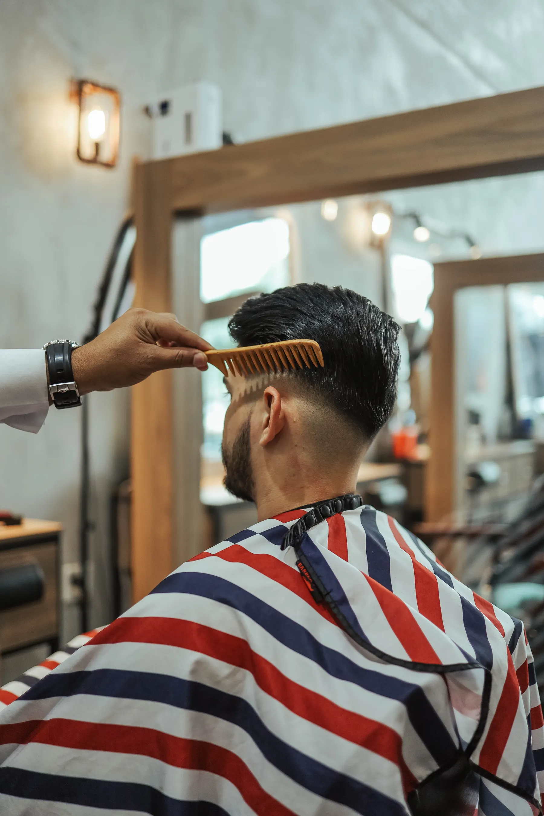 Barber combing a seated client’s hair beside a wooden mirror