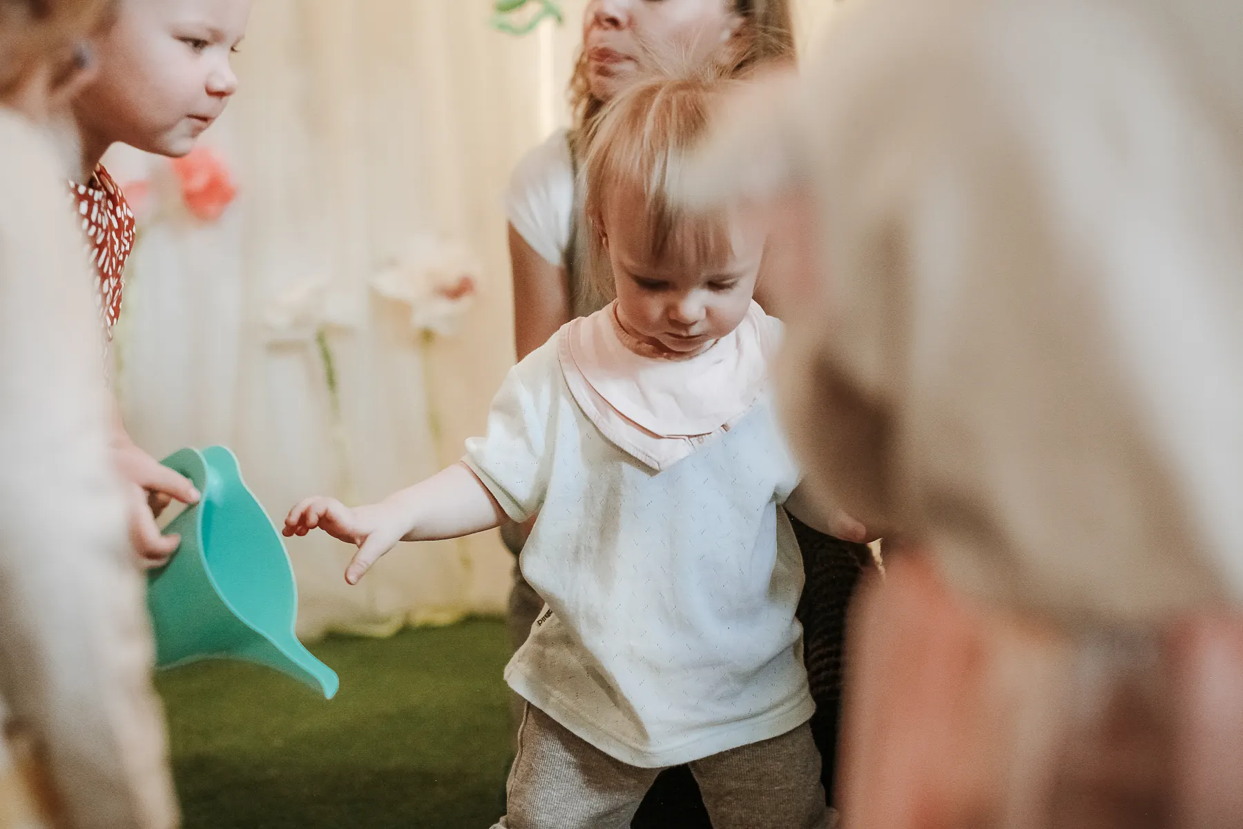 Young child reaching for a green play funnel with others nearby