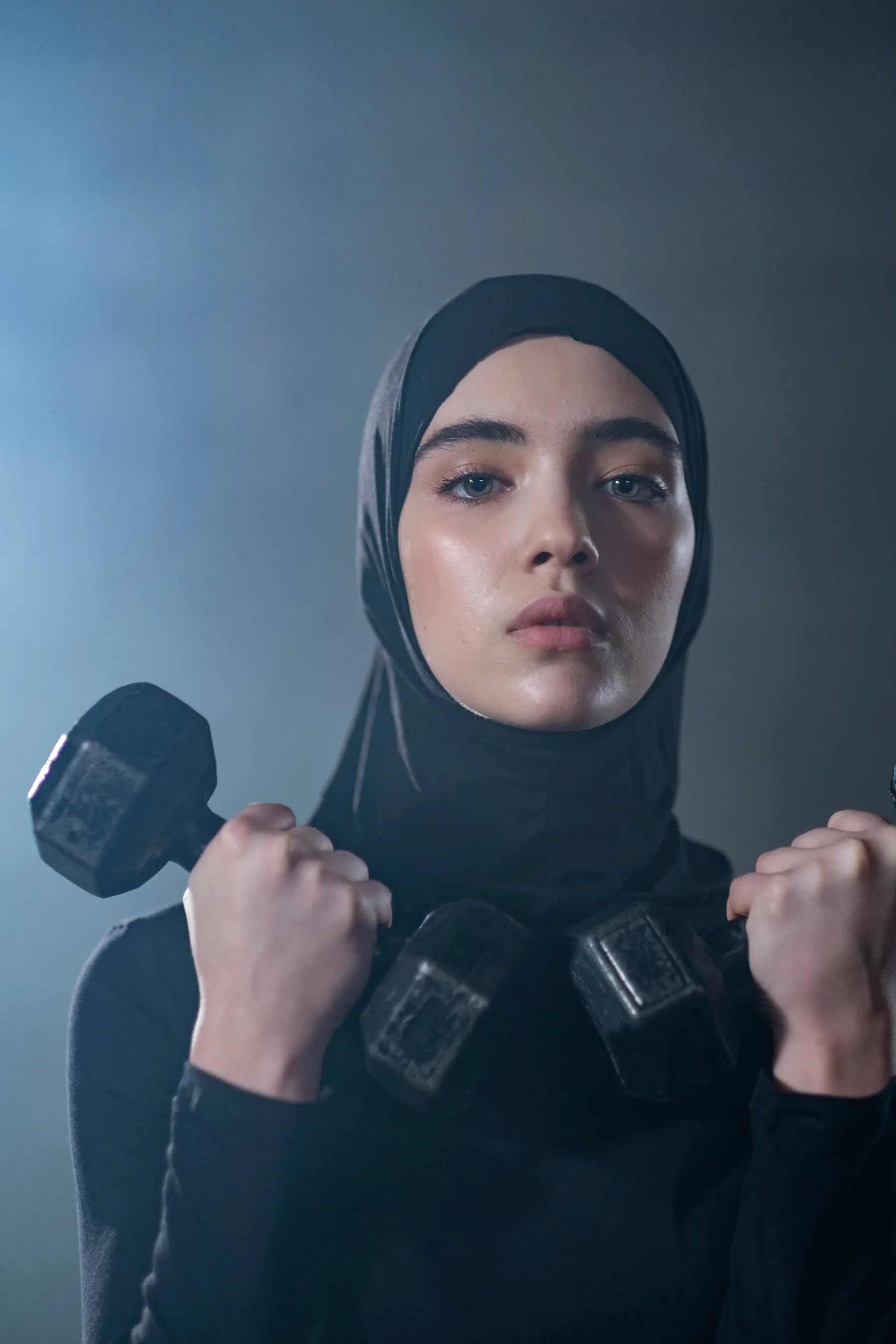 Woman in a black head covering holding dumbbells during exercise