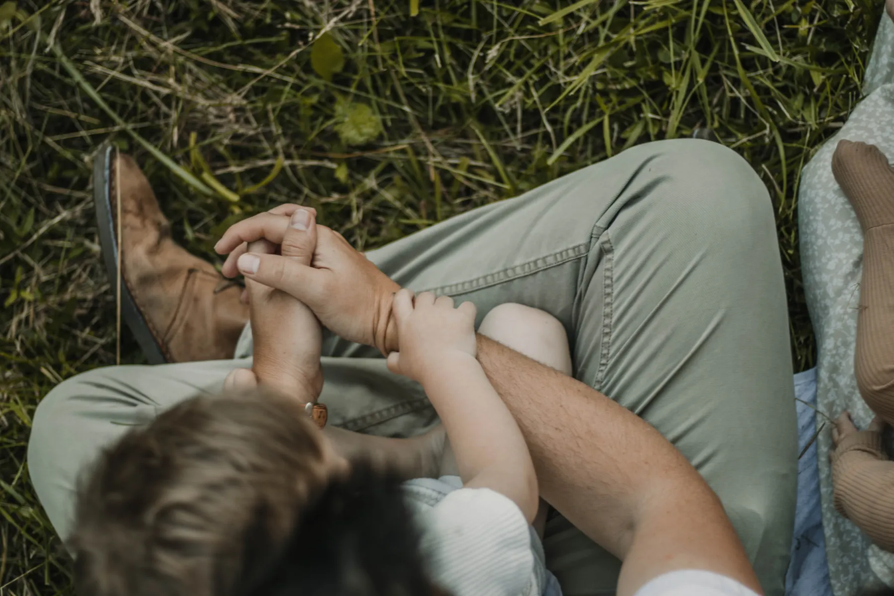 Close view of a child holding a parent’s hand while sitting outdoors