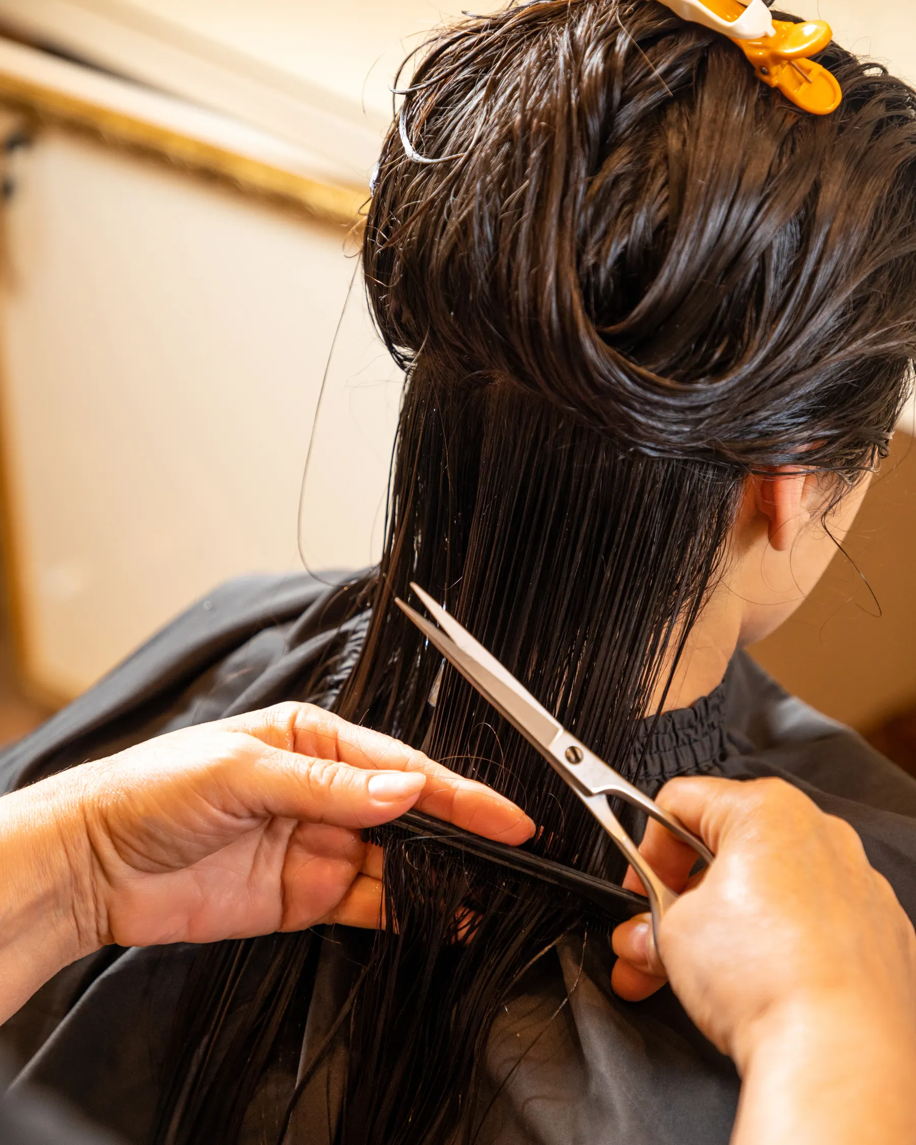 Close view of scissors trimming long hair held with an orange clip