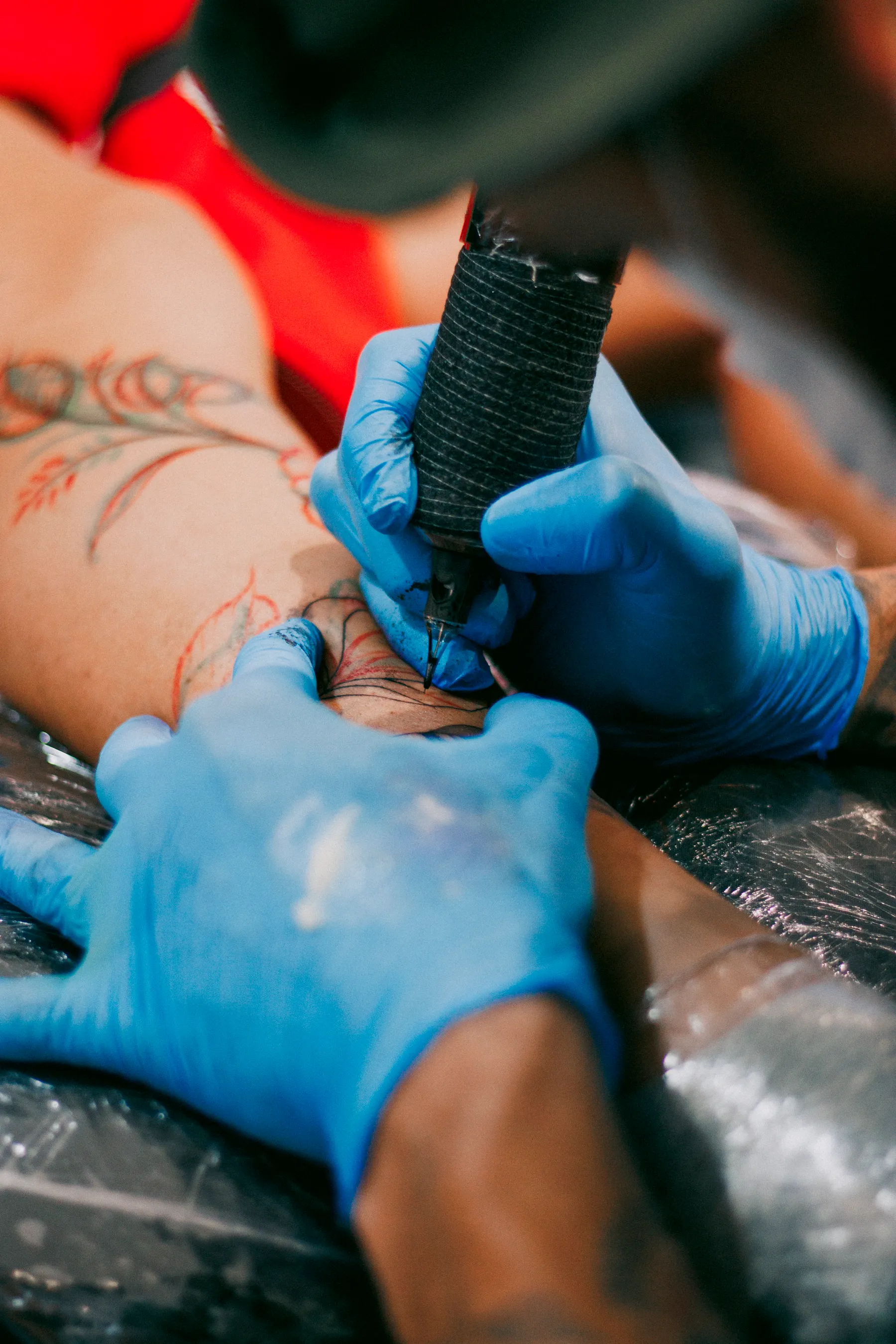 Blue-gloved hands using a tattoo machine on an arm