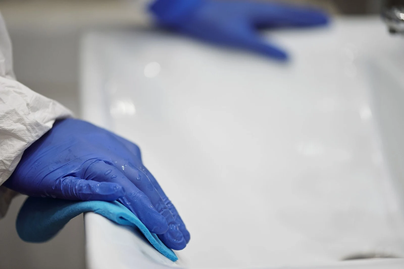 Gloved hand wiping a white bathroom basin