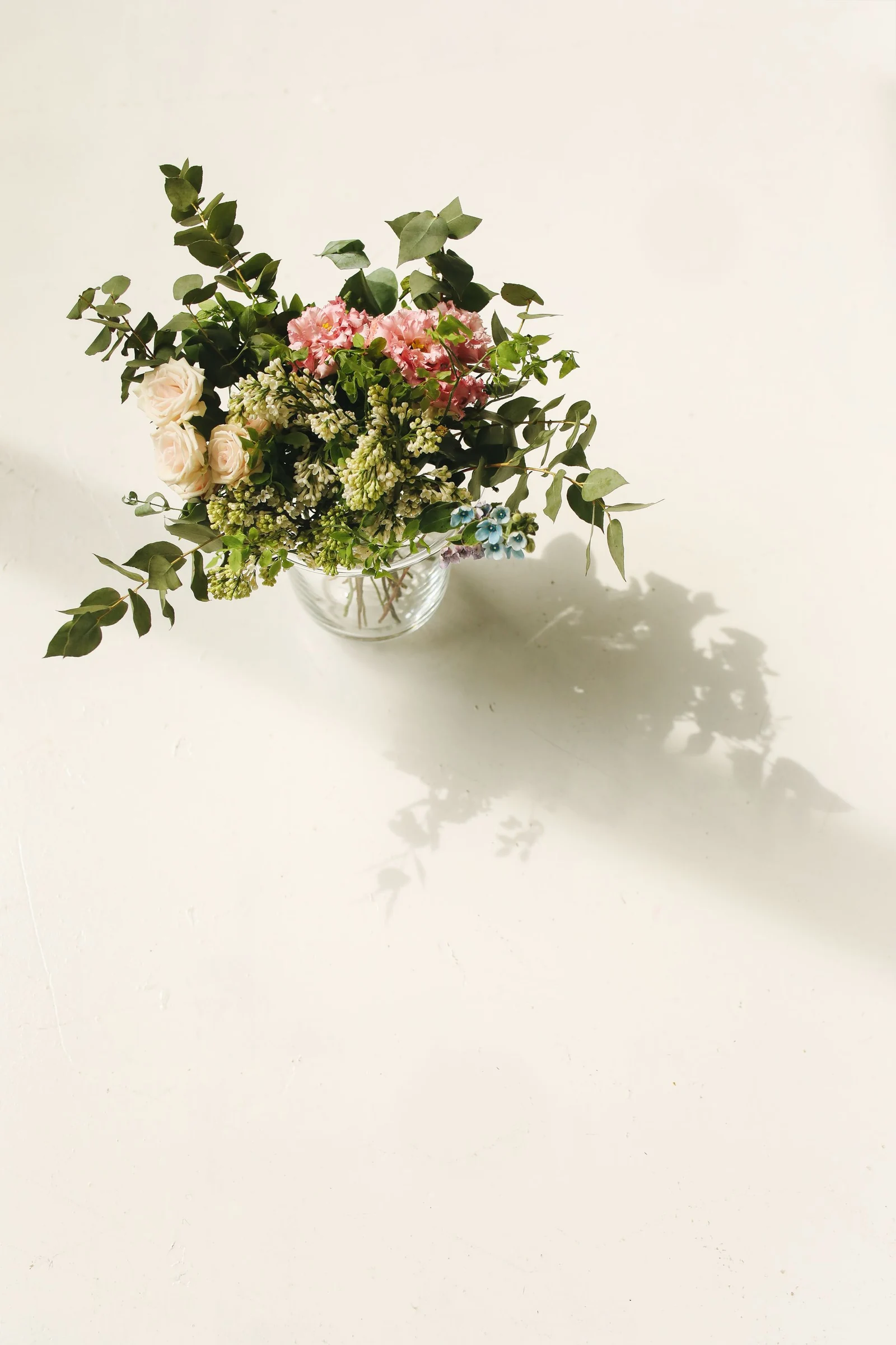 Cream and pink flowers with green foliage arranged in a clear vase