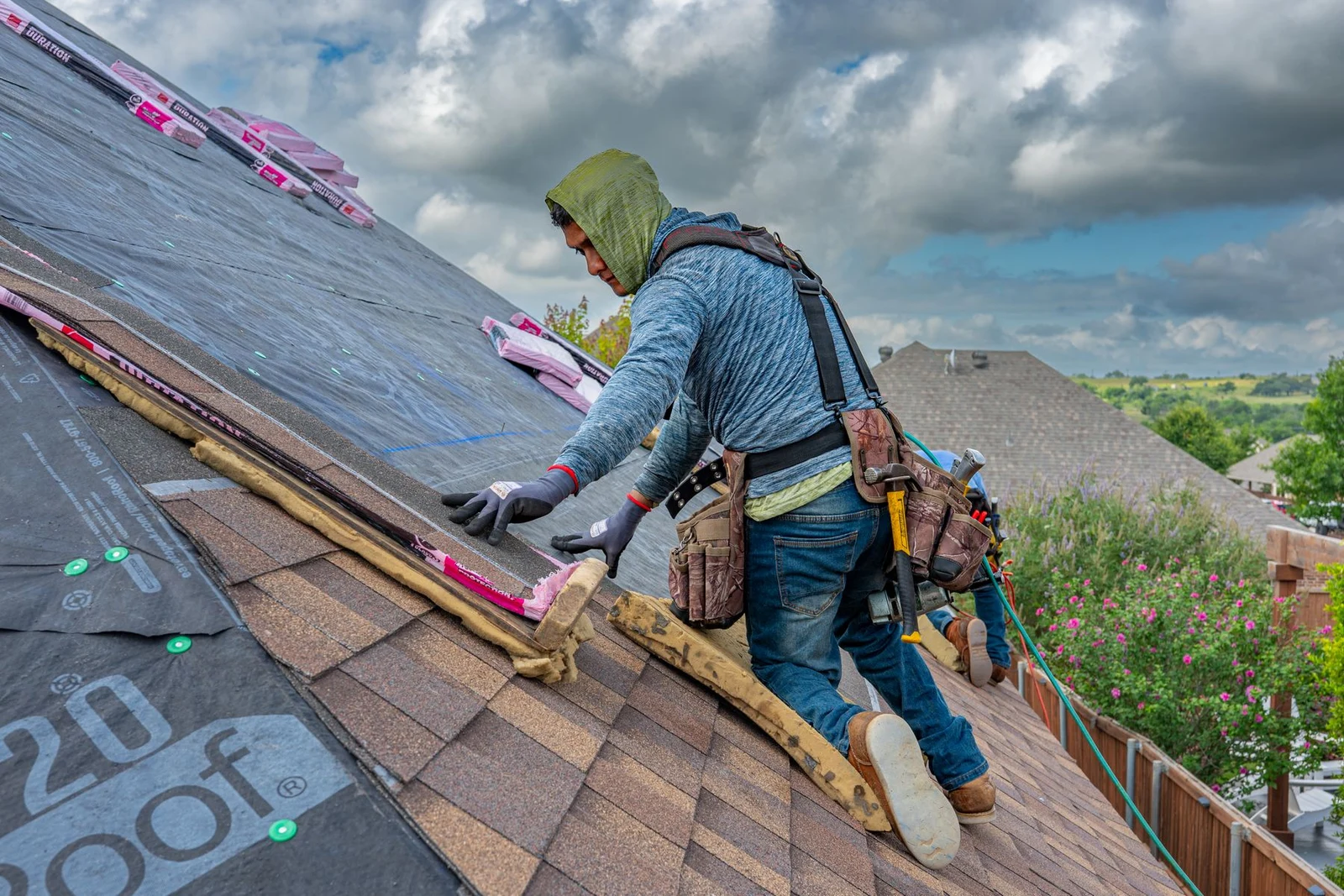 Worker wearing a harness installing asphalt roof shingles